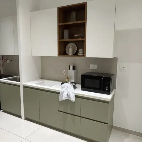 Compact olive-green kitchenette split around a structural column, with a teak open niche of crockery cut into the white wall-unit line and a beige tile band
