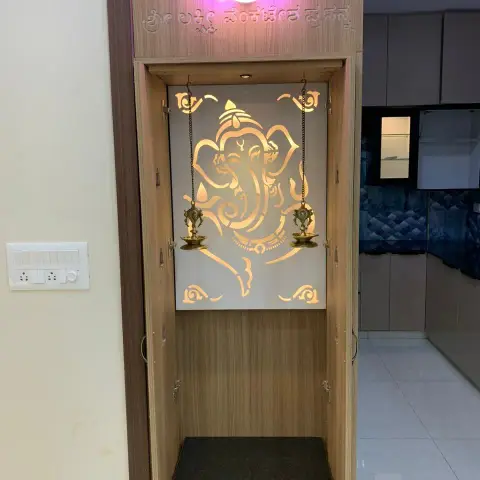 Compact pooja unit with a backlit laser-cut Ganesha jaali panel, wood cabinetry and a granite-top base shelf.