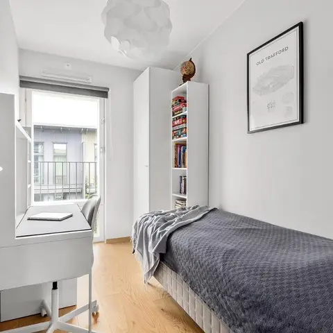Compact single-bed room with a white wardrobe and bookshelf beside a window desk, a sports-themed poster on the wall.