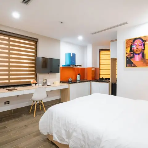 Compact studio flat where a white-quilted bed sits a few feet from an L-shaped kitchenette with a bright orange glass splashback