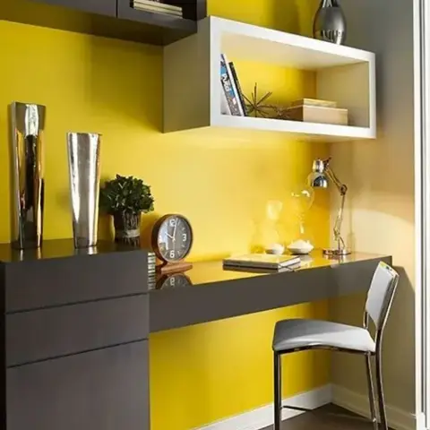 Compact study nook against a chrome-yellow wall: a wall-hung graphite desk that runs into a three-drawer chest, a white open box shelf floating above it