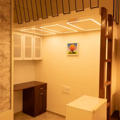 Compact study nook under a loft ladder with a wood-finish desk unit, frosted-glass overhead cabinets and diamond cove-lit ceiling.