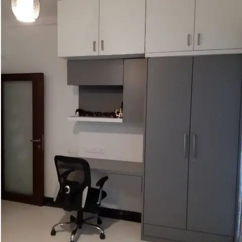 Compact study nook with a white floating desk and open shelf built into a wardrobe unit, black mesh office chair, and a teardrop pendant light overhead.