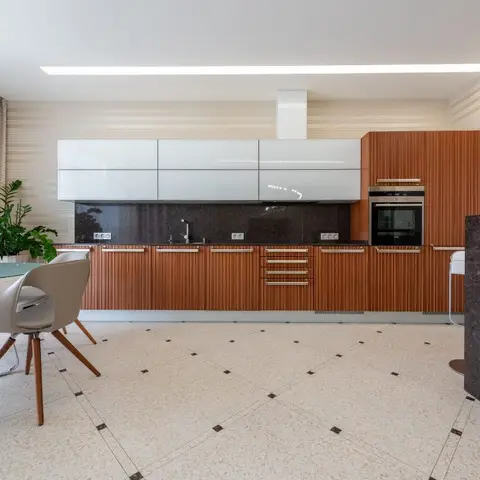 Contemporary kitchen with fluted wood-tone lower cabinets, glossy white uppers, a dark stone backsplash