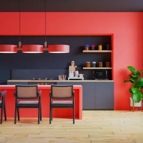 Coral-red and navy colour-blocked kitchen with a red breakfast-bar island, three red drum pendants over it and cane-back black chairs on pale wood flooring.