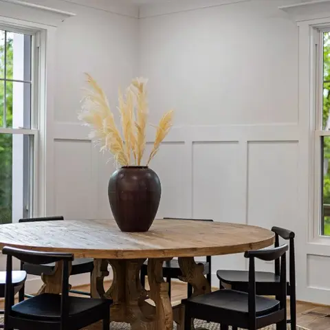Corner dining nook with a round reclaimed-wood pedestal table, black wood dining chairs, board-and-batten wainscoting