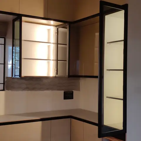 Corner kitchen installation with glossy tan shutters trimmed in black, black-framed glass display cabinets with interior lighting