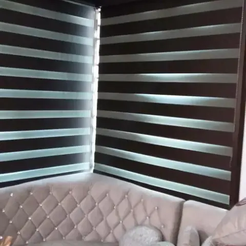 Corner living room seating nook with a diamond-tufted grey sectional sofa beneath dark-brown zebra blinds on two adjoining windows.