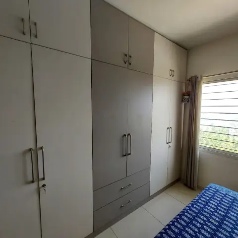 Corner of a bedroom where a two-tone grey and off-white hinged wardrobe run with lofts fills the whole wall
