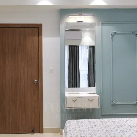 Corner of a bedroom where a duck-egg blue wall carries an ornate-cornered moulding frame next to a full-length dressing mirror with a brass picture light