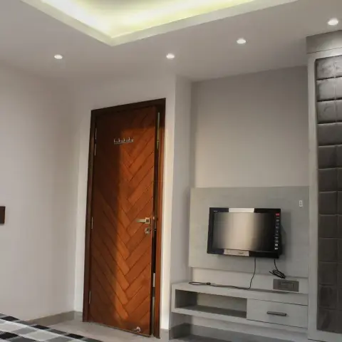Corner of a bedroom with a chevron-veneer teak door, a concrete-grey TV console niche with the cabling run on the surface