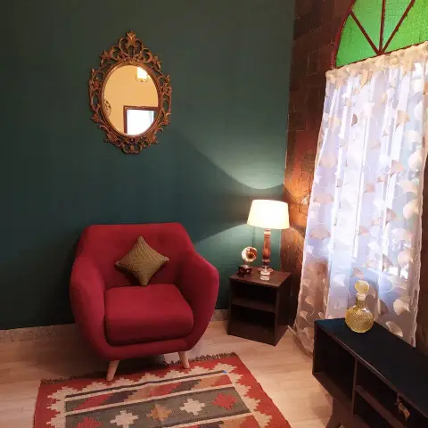 Corner seating vignette with a crimson tub chair on a kilim dhurrie against a bottle-green wall