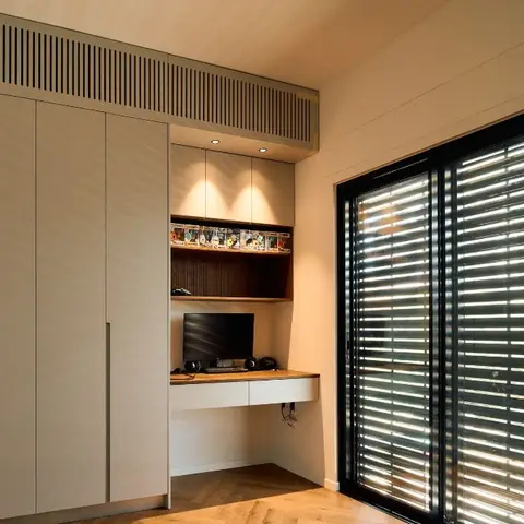 Corner study nook with a floating wood-top desk under a lit display shelf, a textured wardrobe wall, herringbone wood flooring