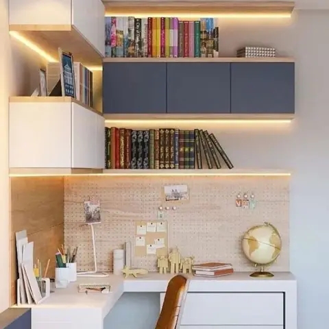 Corner study nook with backlit floating bookshelves in navy and wood, a pegboard desk backsplash styled with pinned photos and notes, a leather desk chair