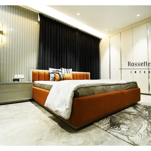 Corner view of a bedroom where a burnt-orange channel-tufted bed stands against greige fluted panelling with a slim brass sconce