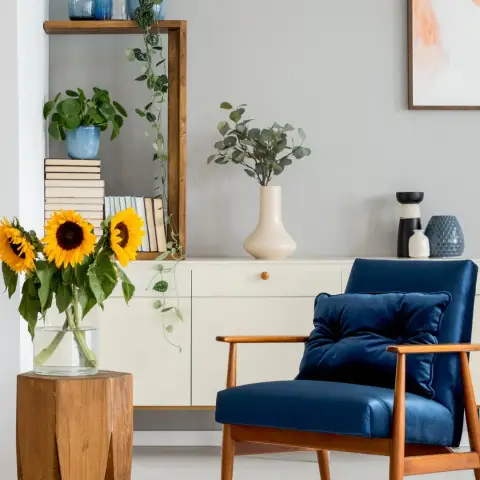 Corner vignette with a navy velvet armchair on a blue quatrefoil rug, a cream sideboard holding blue glass bottles and eucalyptus