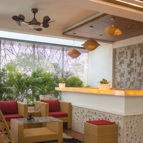 Covered balcony lounge with a hanging rattan swing chair, wicker armchairs in red cushions, a backlit onyx bar counter, and a mother-of-pearl mosaic wall.
