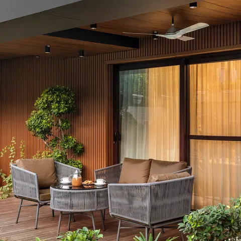 Covered balcony with vertical timber slat wall cladding, wood decking, and a grey woven-rope outdoor seating set around a round coffee table.