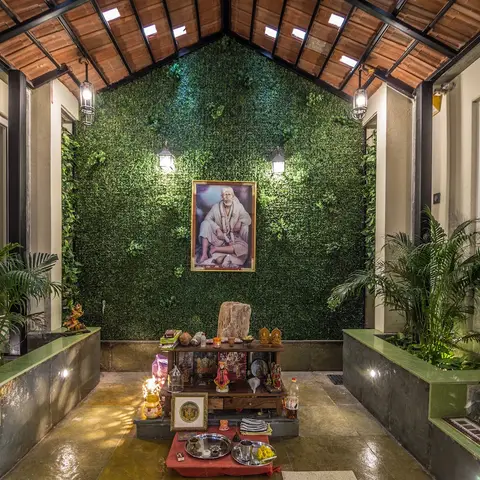Covered courtyard leading to a pooja altar, framed by a full-height artificial green wall and a pitched clay-tile skylight roof.