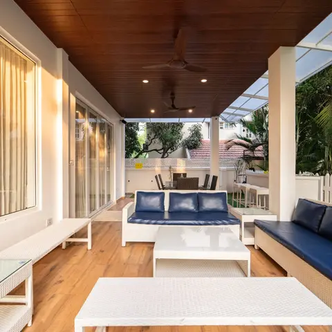 Covered villa balcony with a wood-plank ceiling and ceiling fans, furnished with white rattan sofas, benches and coffee tables in navy cushions