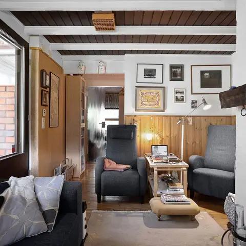 Cozy cabin-style living room with a dark wood beamed ceiling, pine wall panelling, a navy sofa with floral cushions