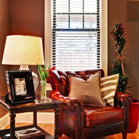 Cozy reading corner with a tufted brown leather armchair, a dark wood side table with a lamp and framed photo, and a patterned rug on wood flooring.