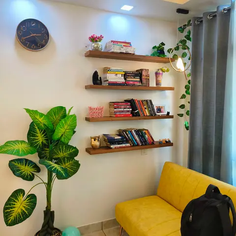 Cozy reading corner with four dark-wood floating shelves stacked with books and curios, a mustard-yellow sofa