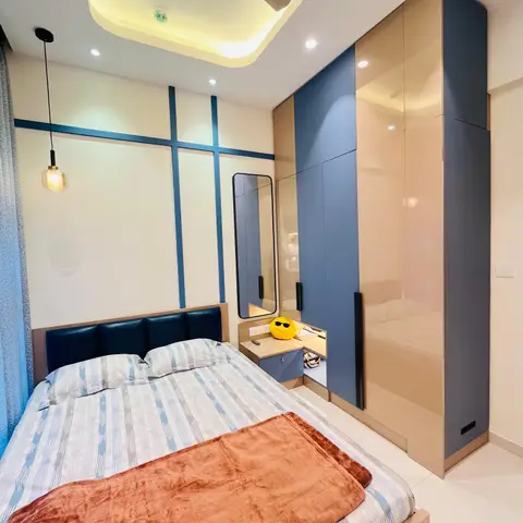 Cream bedroom where thin navy inlay strips cross the headboard wall in a grid, facing a two-tone blue and champagne gloss wardrobe with a tall mirror over a