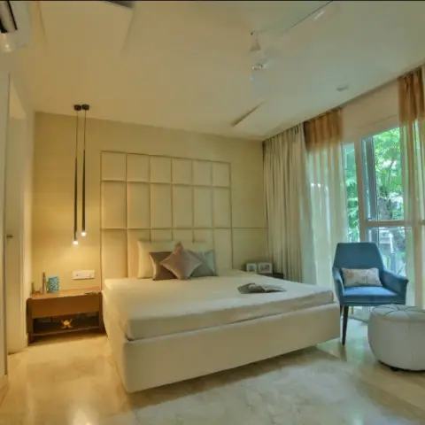 Cream bedroom with a grid-tufted upholstered headboard panel carried wall to wall, slim black cylinder pendants dropped over a floating bedside shelf