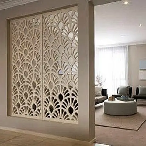Cream carved jaali screen panel with a floral fan motif framing the entrance to a living room with a grey sofa and round tufted ottoman beyond.