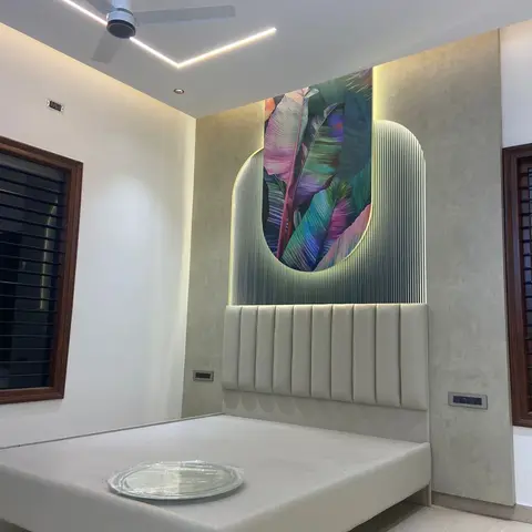 Cream channel-tufted headboard under an arched fluted panel cut away to reveal a jewel-toned banana-leaf mural, with a V-shaped linear ceiling light and a fan