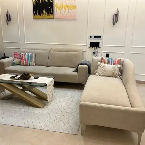 Cream fabric sofa with a matching chaise on an ivory diamond flatweave rug, against a white applied-moulding wall hung with two abstract canvases and slim