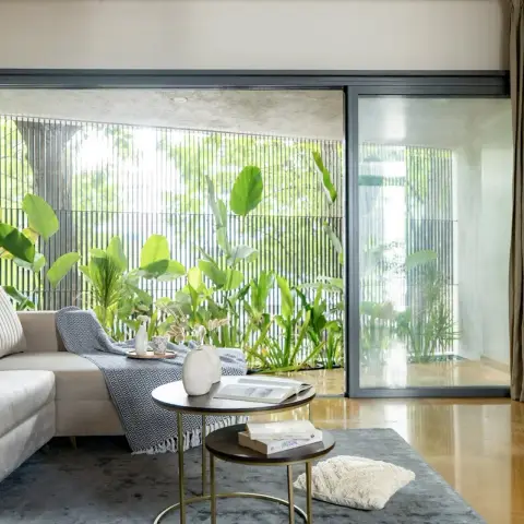 Cream fluted-back sectional and a pair of nesting brass-legged tables set against full-height sliding glazing onto a planted courtyard screened by vertical