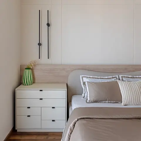 Cream grid-panelled wall with two slim black wand sconces at staggered heights above a pale-oak headboard ledge
