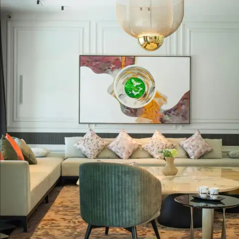 Cream L-shaped low sofa with blush patterned cushions runs under a large abstract canvas of green birds in a white bowl