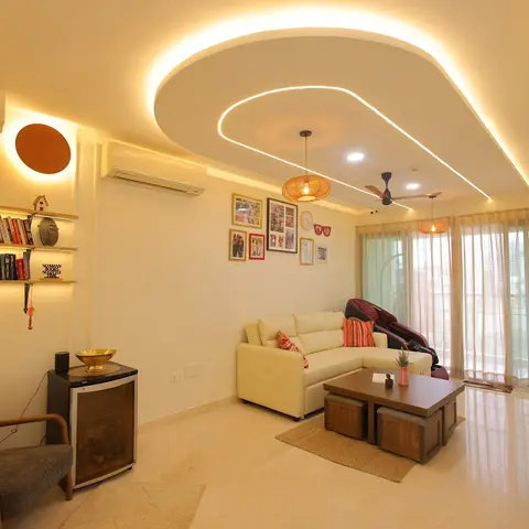 Cream L-shaped sofa and wood coffee table with cube stools under a curved cove-lit false ceiling with rattan pendant lights