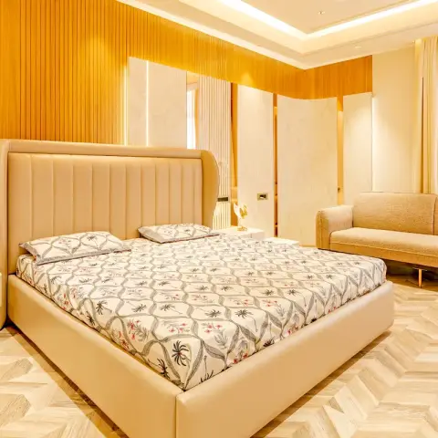 Cream leather bed with a curved channel-tufted headboard against a honey-toned fluted wood wall, floating white bedside slabs either side