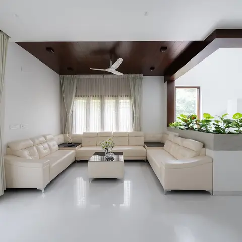 Cream leather U-shaped sectional facing a windowed living room with dark wood plank ceiling and a built-in planter dividing a staircase landing beyond.