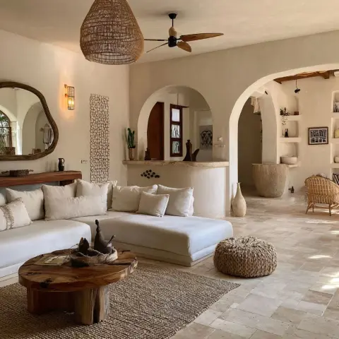 Cream lime-plastered living room where two rounded masonry archways open off a low white platform sofa, with a live-edge round wood coffee table