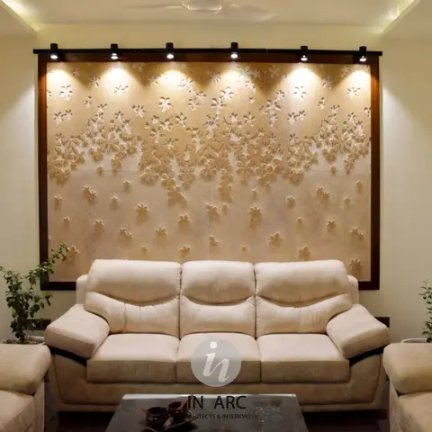Cream living room dominated by a large carved floral stone feature wall lit by a spotlight track, framed by matching sofas around a glass coffee table.