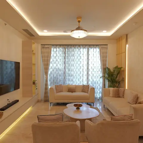 Cream living room with two sofas and armchairs around a round marble coffee table, patterned sheer curtains, and a gold-textured wallpaper accent wall.