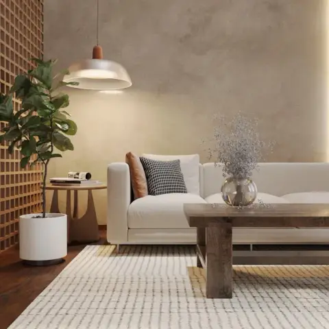 Cream low-back sofa against a warm lime-plaster wall with a concealed light slot, faced by a chunky reclaimed-wood plank table on a ribbed ivory rug