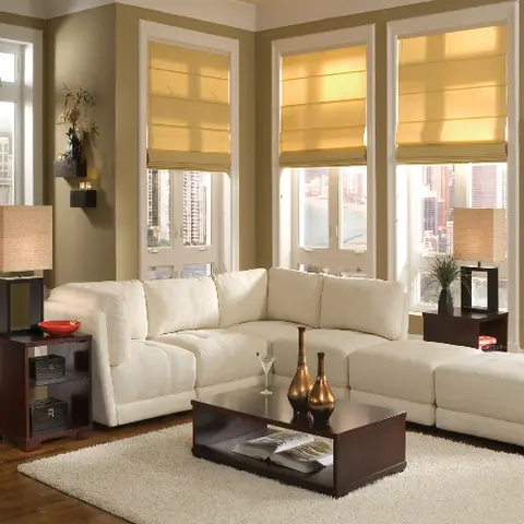 Cream sectional sofa living room with dark wood side tables and coffee table, gold roman shades and a city skyline view through corner windows