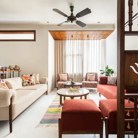 Cream teak-framed sofa and terracotta velvet ottomans around twin marble-top tables on a striped cotton dhurrie