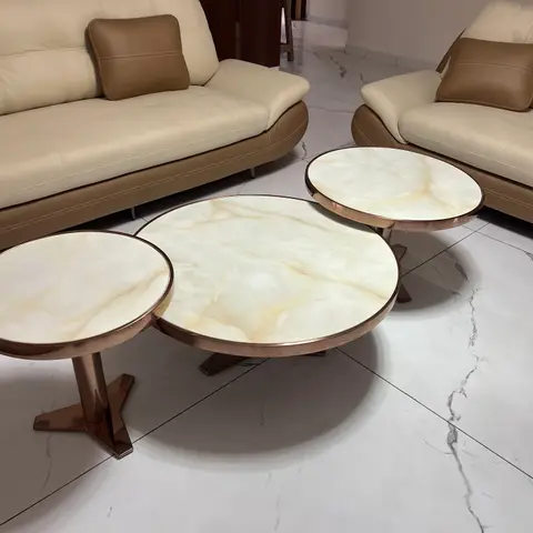 Cream tufted leather sofas around a cluster of round marble-top coffee tables with rose-gold metal frames on a marble floor.