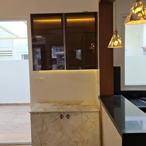 Crockery unit with amber fluted-glass shutters in slim bronze frames sitting over a marble-print laminate base cabinet, LED-lit top and bottom