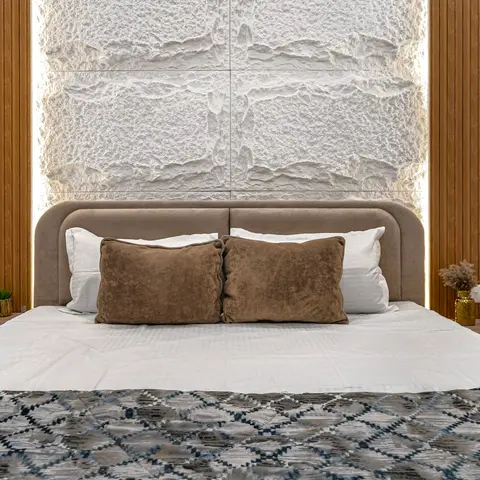 Curved beige suede headboard set against a backlit rough-split white stone-clad panel