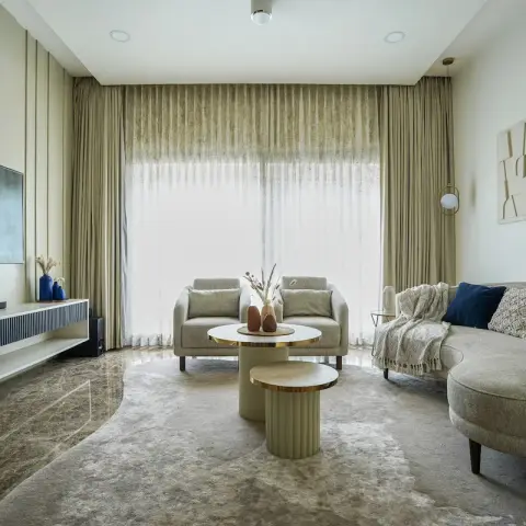 Curved bone-linen sofa and two boxy armchairs face a beige fluted TV wall with brass reveals