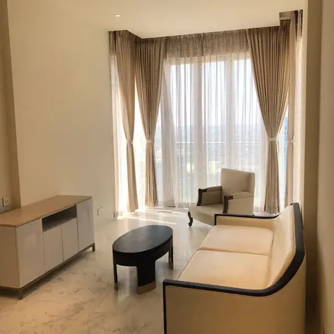 Curved cream sofa with black piping beside an oval black coffee table, floor-to-ceiling sheer curtains framing a skyline view.