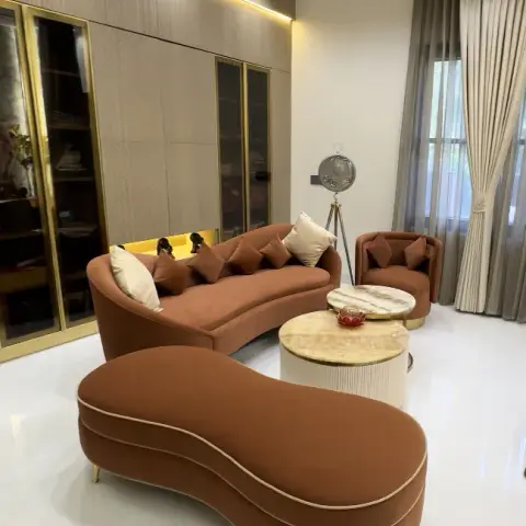 Curved rust velvet sofa with a peanut-shaped bench in front of it, round marble and fluted side tables between